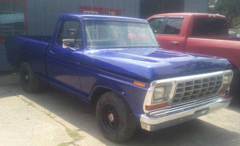 Late-1970s Ford pickup in bright blue paint with a chrome grille and black wheels, a red truck behind it