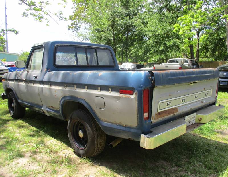 Older two-tone blue and silver Ford pickup from the rear, faded paint with rust, parked on grass