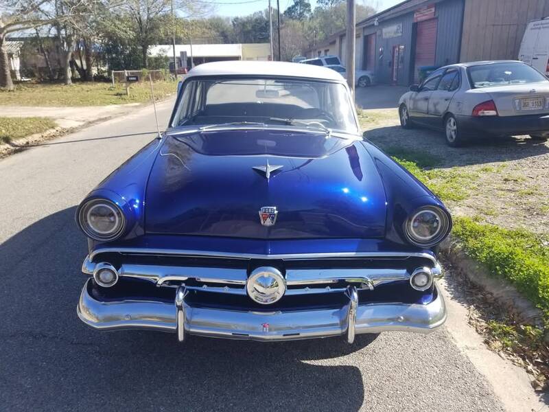 Front of a 1950s Ford sedan in glossy deep-blue paint with a white roof, chrome bumper and grille, parked on a street