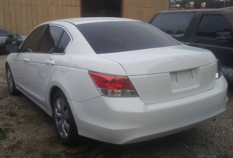 White Honda Accord sedan seen from the rear corner, parked on gravel by a wooden building
