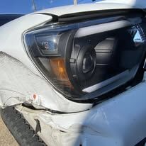 White Toyota Tacoma front corner with a crumpled bumper and fender and scraped paint by the headlight